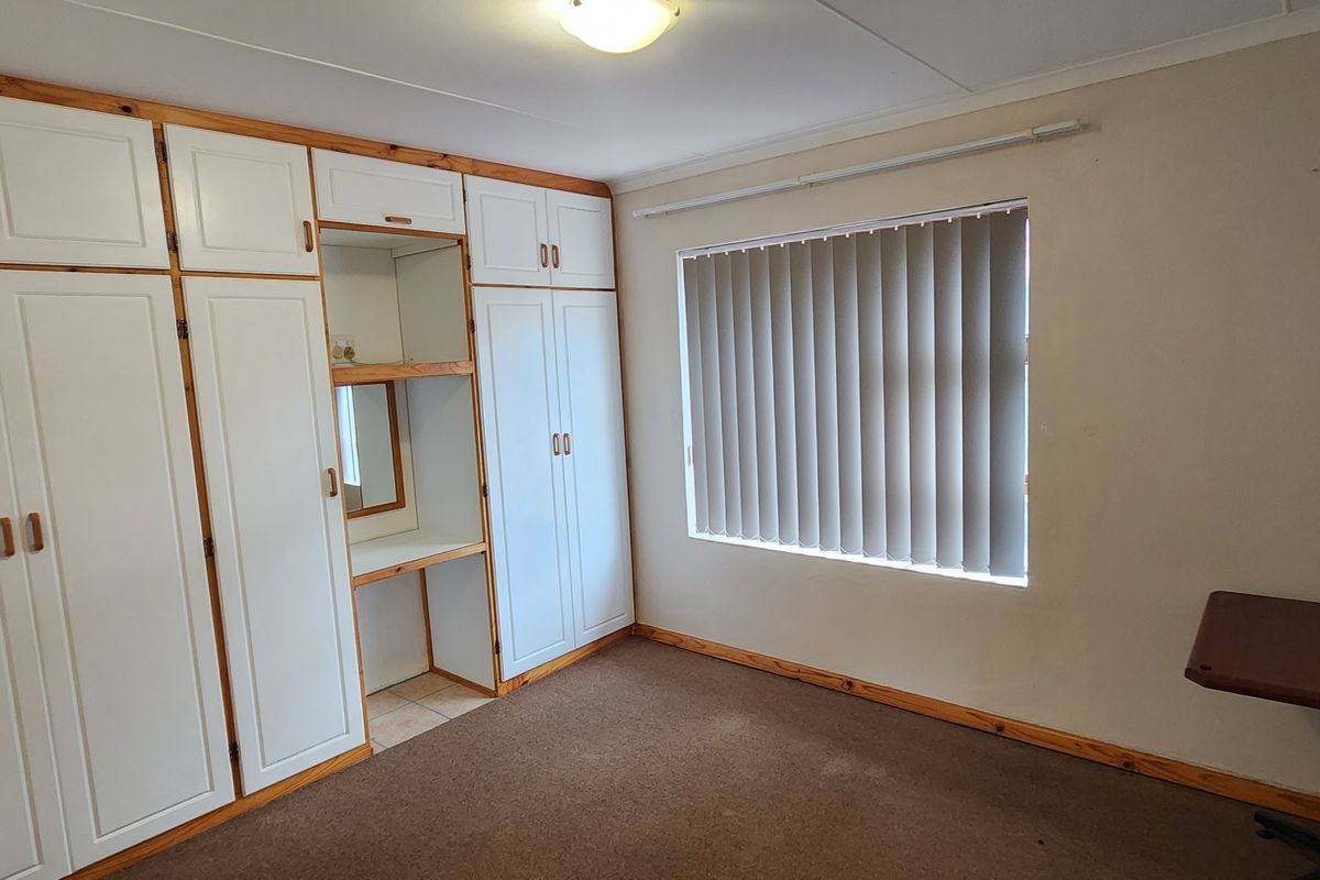 A bedroom featuring extensive built-in white cabinetry with integrated vanity and vertical window blinds.