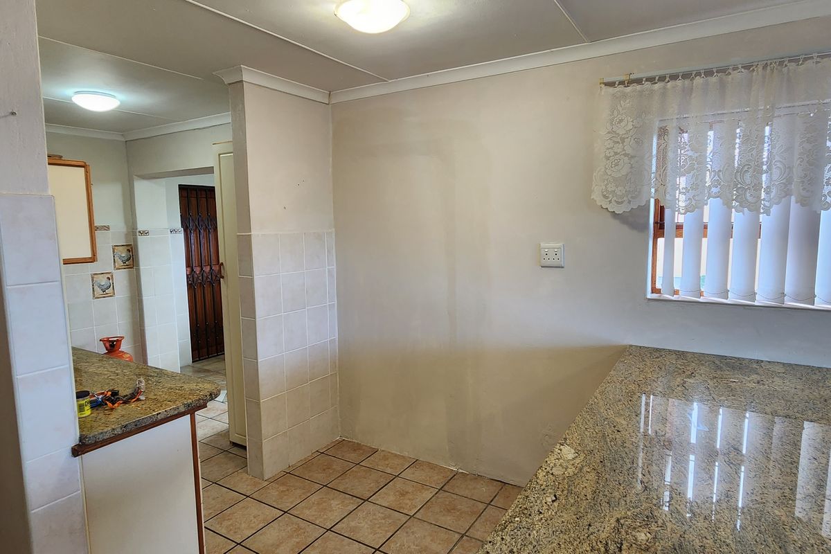 A functional kitchen area featuring granite countertops, tiled flooring, and a pass-through window, offering a practical layout for daily meal preparation.