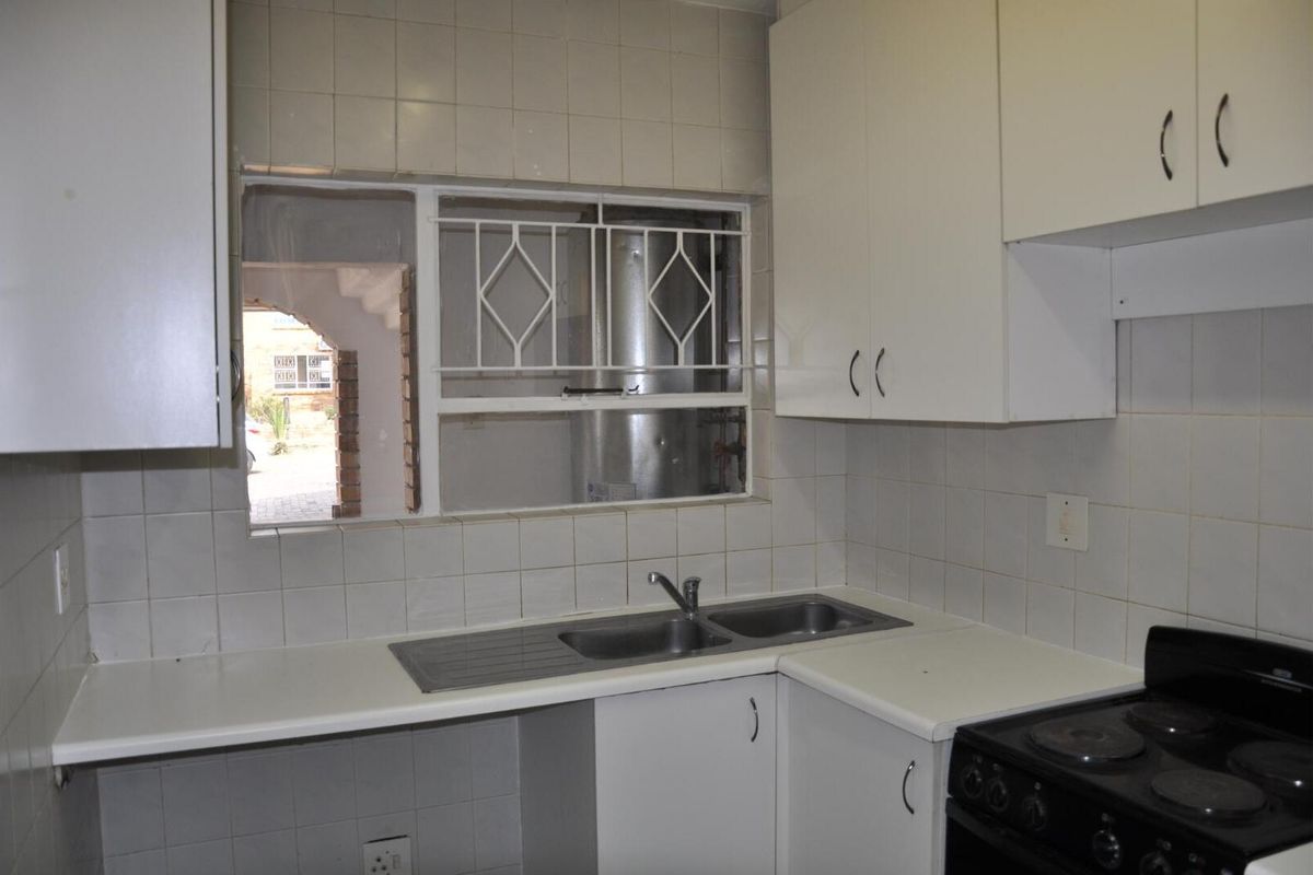 A compact kitchen featuring white cabinetry, a double-basin stainless steel sink, and a built-in electric stove, with tiled splashbacks and a window view.