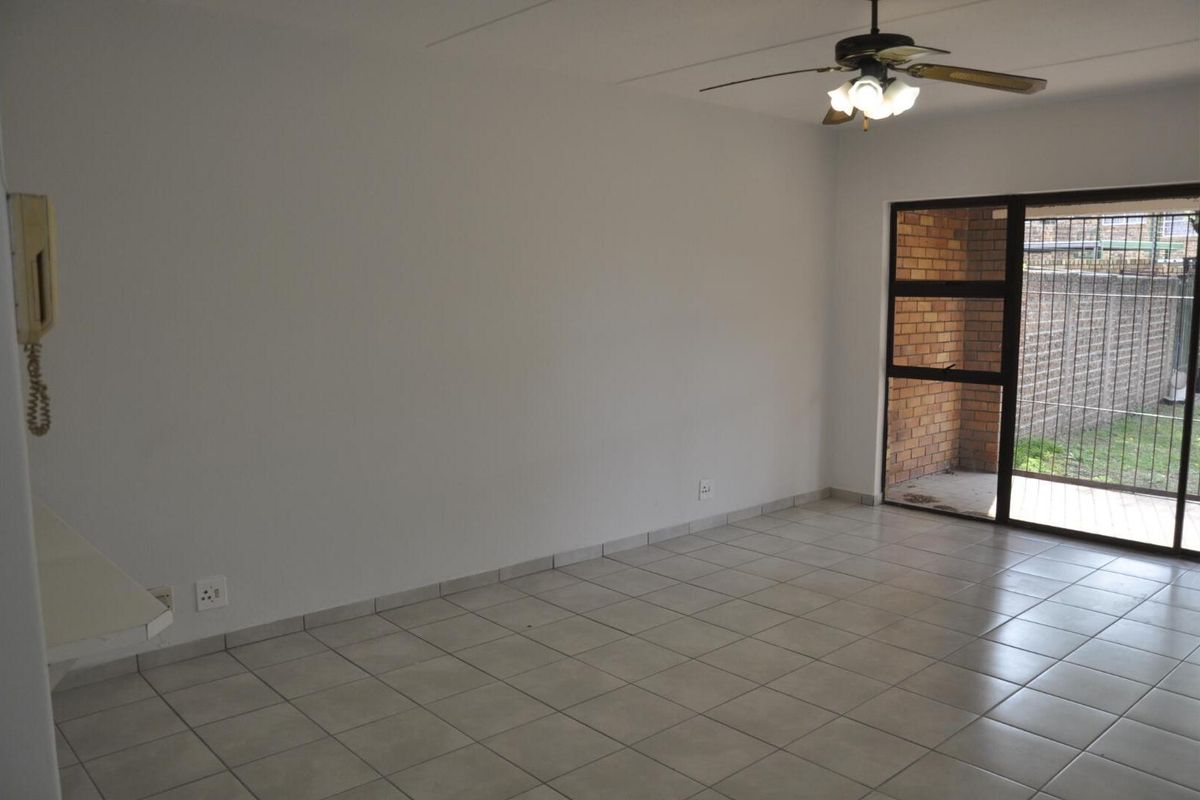 An empty living room featuring tiled flooring, a ceiling fan, and a sliding glass door providing access to an outdoor patio area.