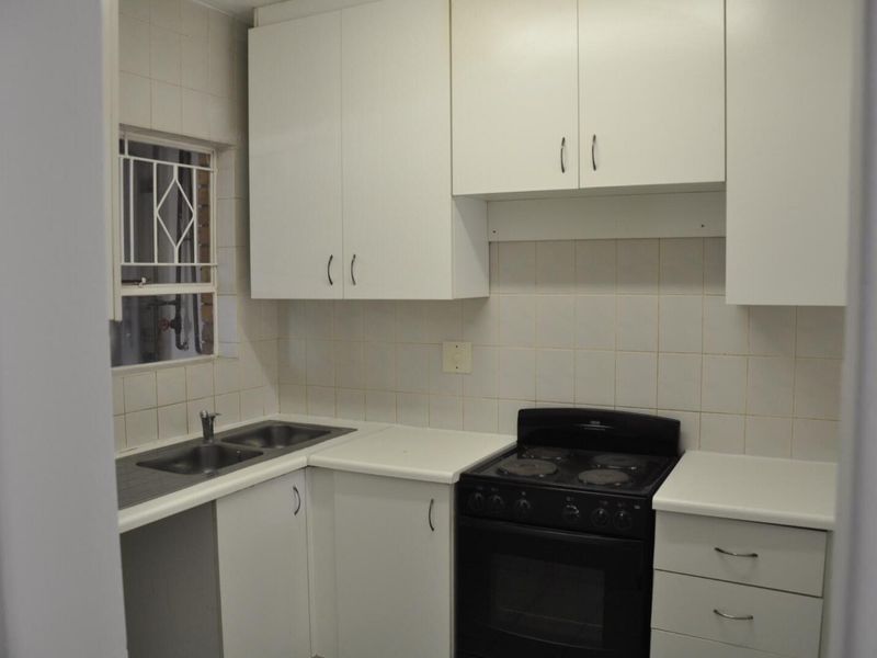A functional kitchen featuring white cabinetry, tiled splashbacks, a double basin sink, and a freestanding electric stove.