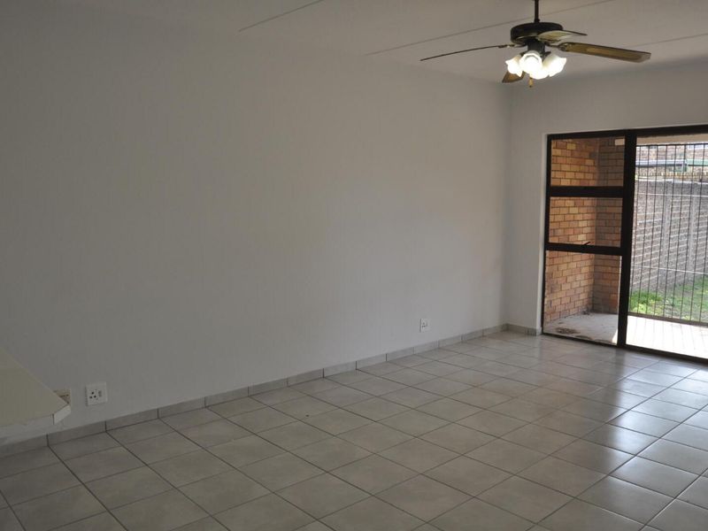 An empty living room featuring tiled flooring, a ceiling fan, and a sliding glass door providing access to an outdoor patio area.