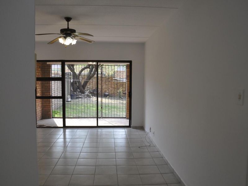An open-plan living area featuring tiled flooring, a ceiling fan, and large sliding glass doors providing access to the rear garden.