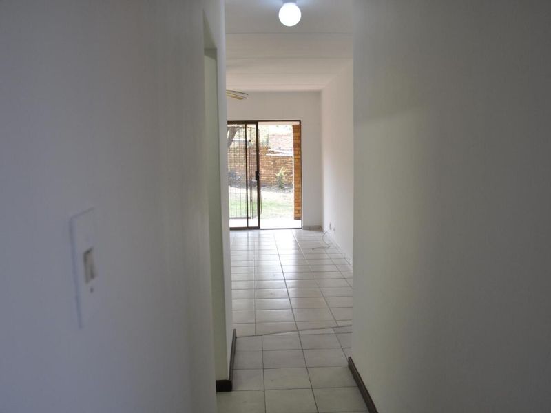 A view through a hallway leading into an open-plan living area with tiled flooring and a sliding glass door opening to the exterior.