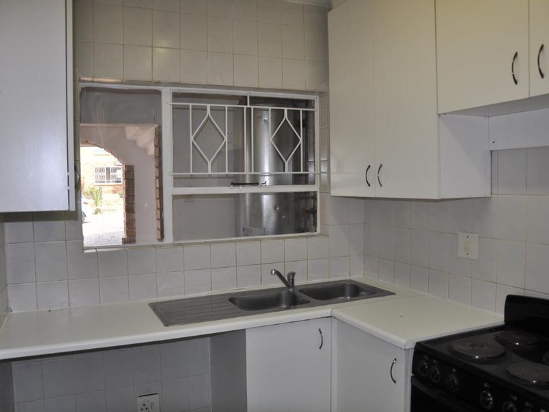 A compact kitchen featuring white cabinetry, a double-basin stainless steel sink, and a built-in electric stove, with tiled splashbacks and a window view.