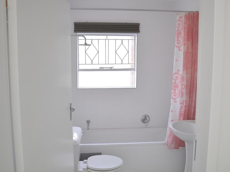 A functional bathroom featuring a white bathtub, pedestal basin, toilet, and a window with security bars.