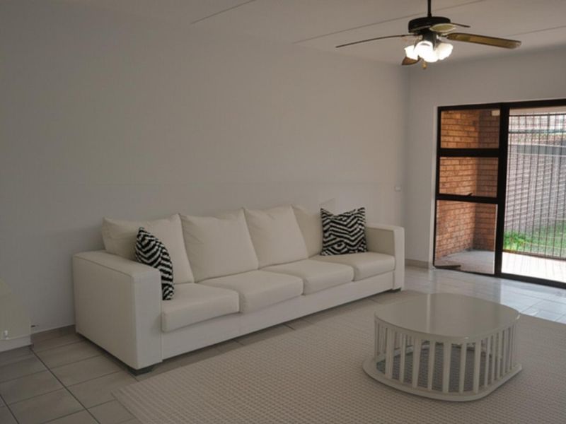 A bright living room featuring tiled flooring, a ceiling fan, and large glass sliding doors providing access to an outdoor area.
