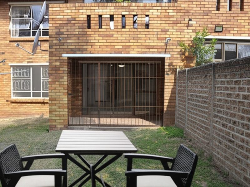A rear view of the apartment featuring a private garden area, brick facade, and secure metal security gate over the entrance.