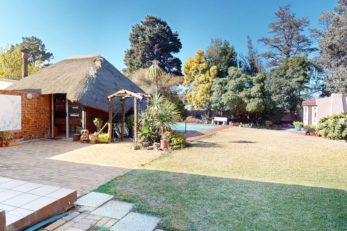 Spacious rear garden featuring a swimming pool, paved patio area, and a traditional thatch-roofed structure, offering a private outdoor entertainment space.