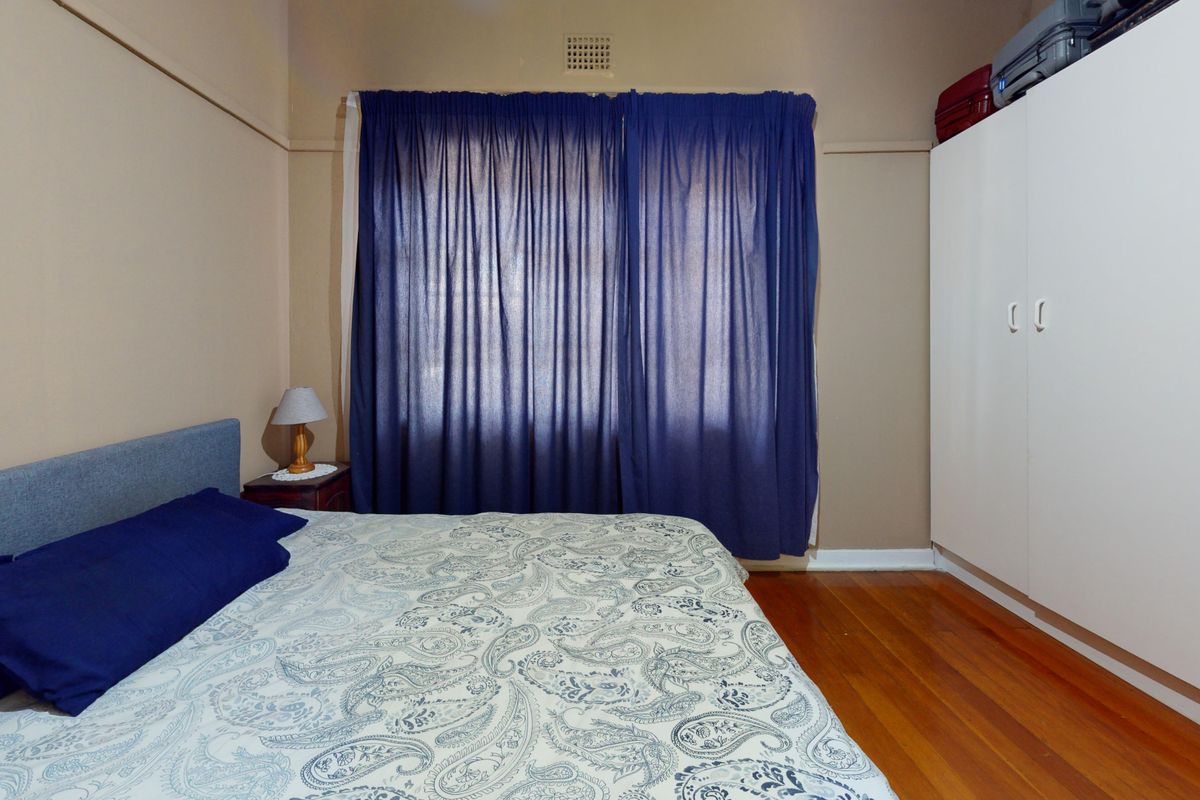 A bedroom featuring polished timber flooring, a built-in wardrobe, and a classic picture rail, offering a functional and well-maintained living space.