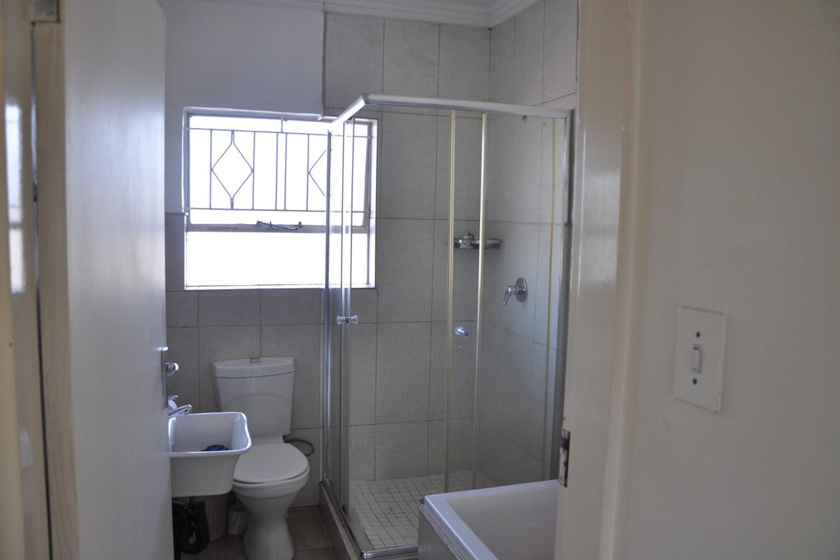 A functional bathroom featuring a tiled shower enclosure, a standard toilet, and a wall-mounted basin with natural light from a window.