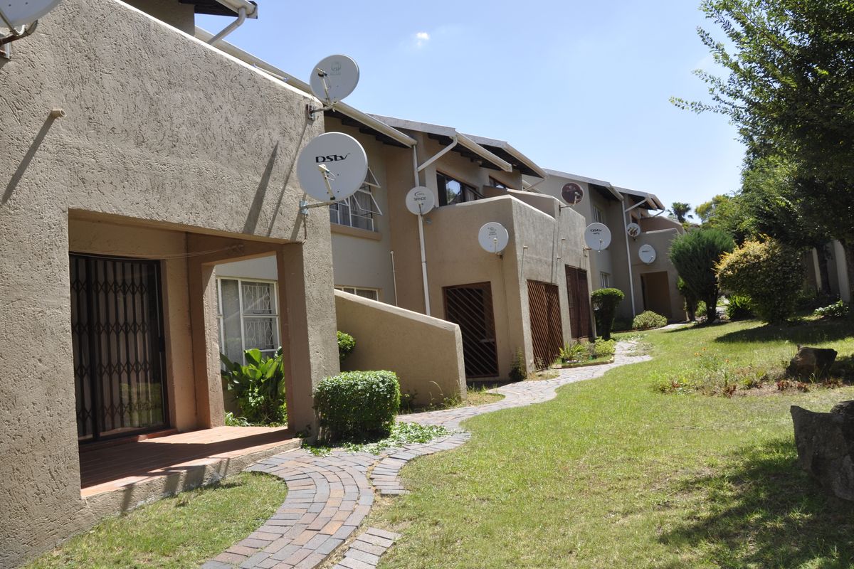 Exterior view of apartment units featuring private patio areas, paved walkways, and shared garden space.