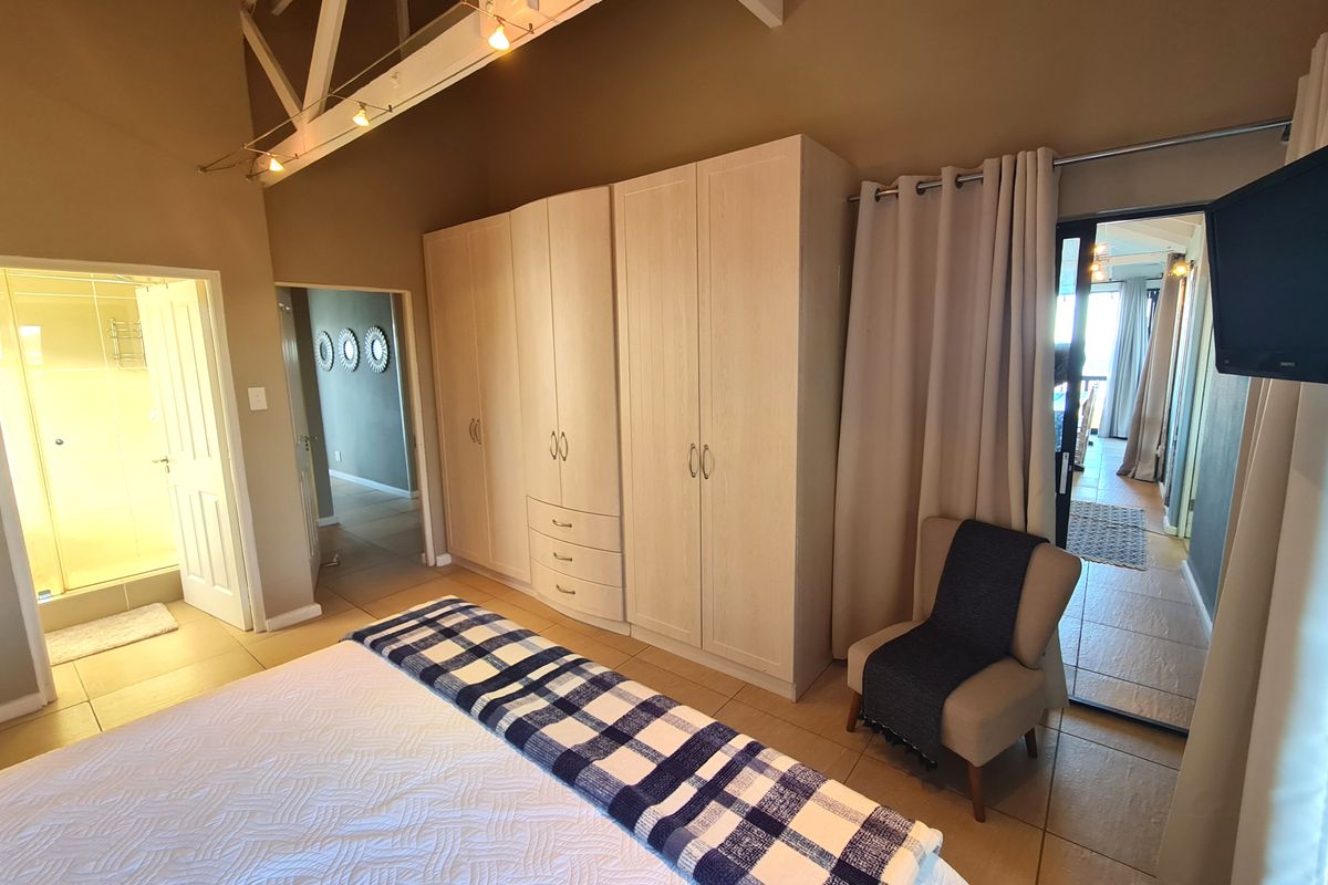 Spacious bedroom featuring vaulted ceilings with exposed trusses, built-in wardrobes, tiled flooring, and direct access to an en-suite bathroom.