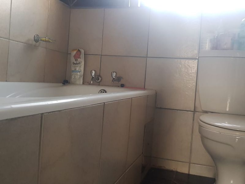A compact bathroom featuring a standard bathtub and toilet with tiled wall finishes, requiring cosmetic updates to improve the overall aesthetic.