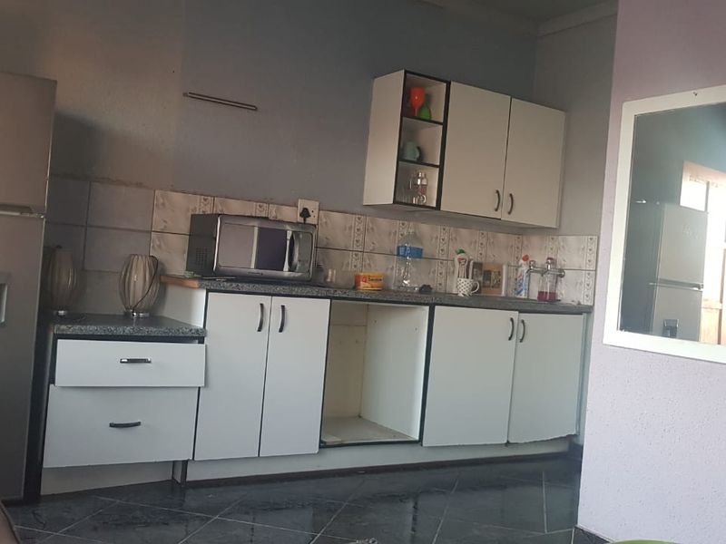 A compact kitchen featuring white cabinetry, tiled backsplash, and dark floor tiles, currently showing signs of wear and missing cabinet hardware.