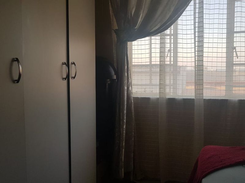 A bedroom featuring a built-in wardrobe and a window with security bars, offering natural light and a view of the surrounding area.