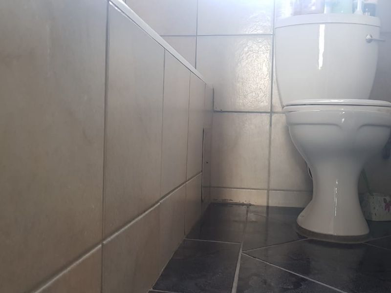 A compact bathroom featuring a standard toilet and a tiled bathtub surround with neutral wall and dark floor tiling.