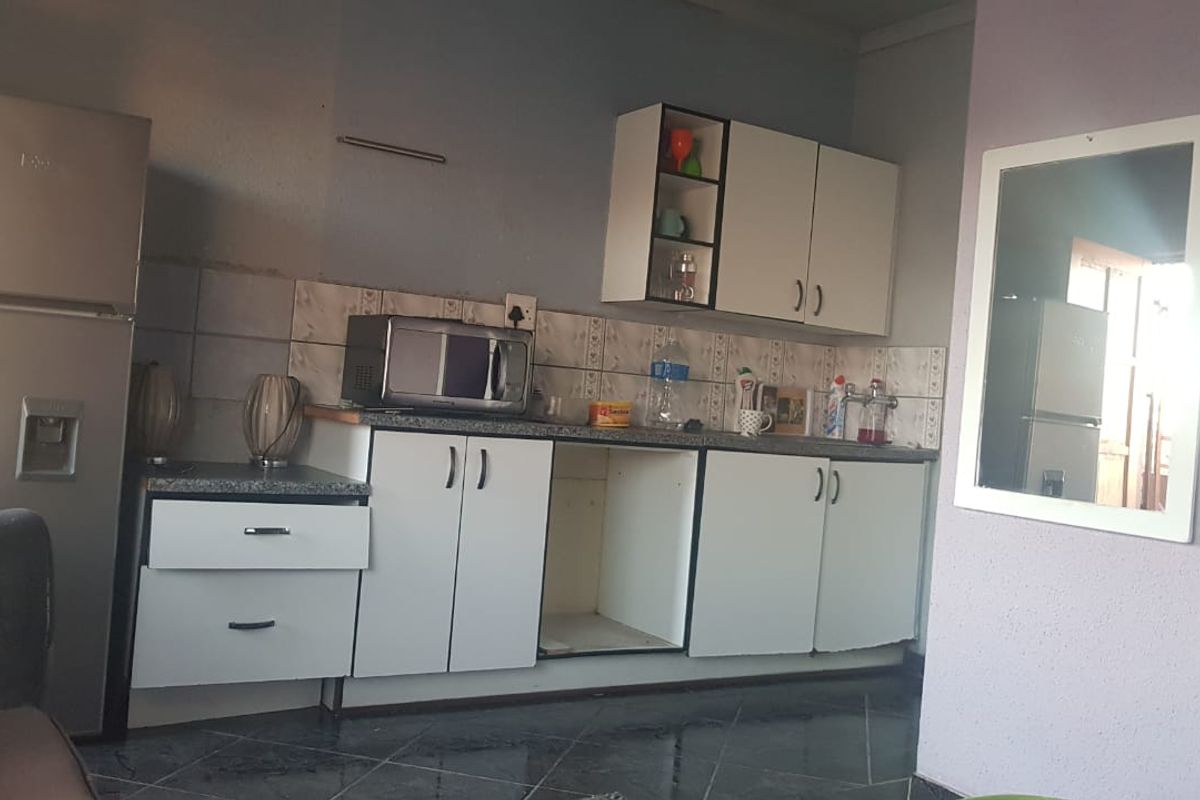 A compact kitchen featuring white cabinetry, tiled backsplash, and dark floor tiles, currently showing signs of wear and missing cabinet hardware.