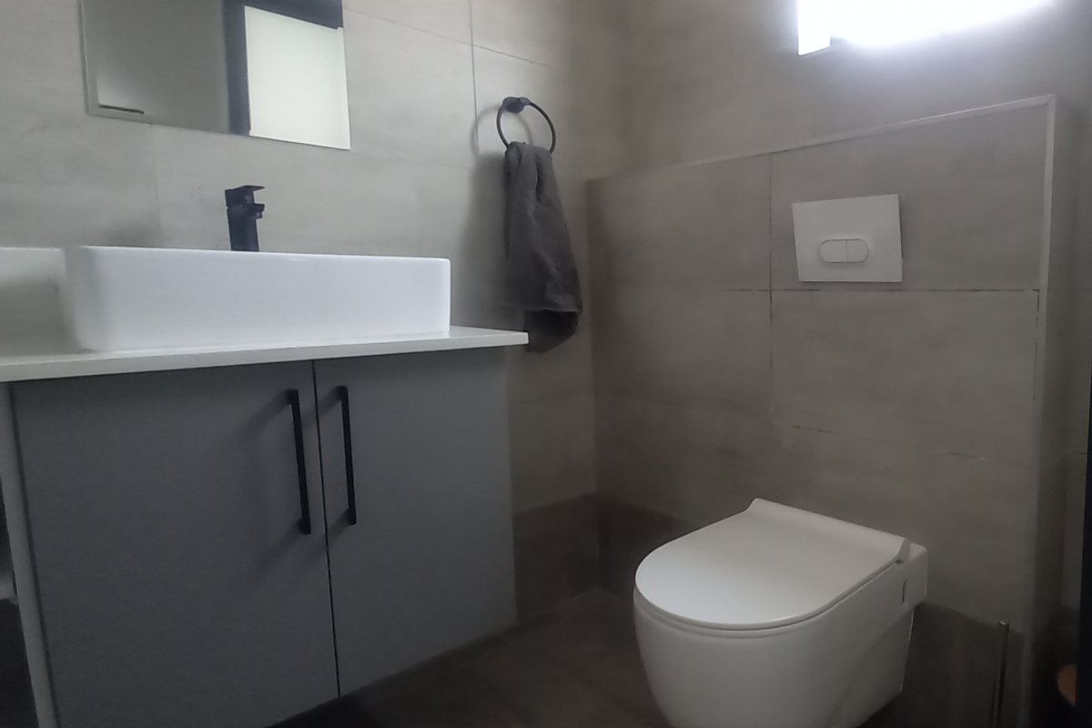 Modern bathroom featuring a wall-mounted toilet with concealed cistern, a contemporary vanity unit with a vessel sink, and neutral wall tiling.