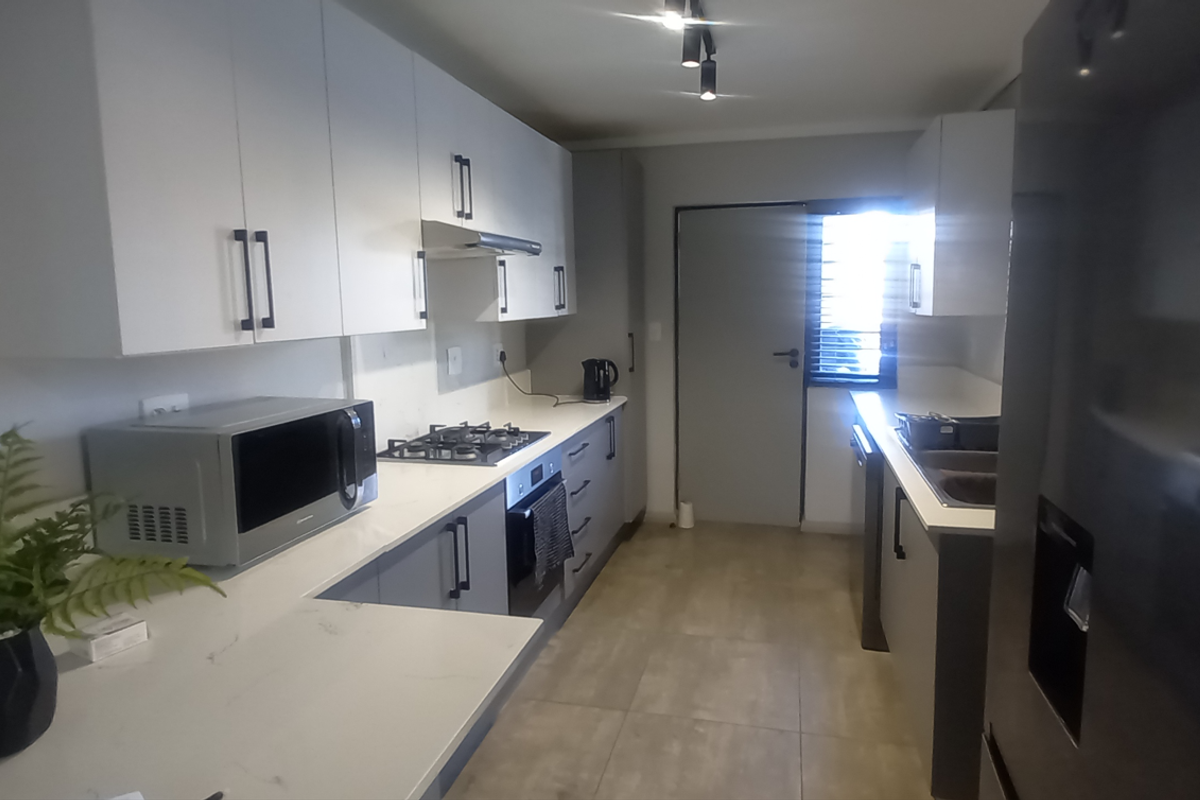 Modern kitchen featuring white cabinetry, stone countertops, built-in gas hob, oven, and extractor fan with tiled flooring and direct access to the exterior.