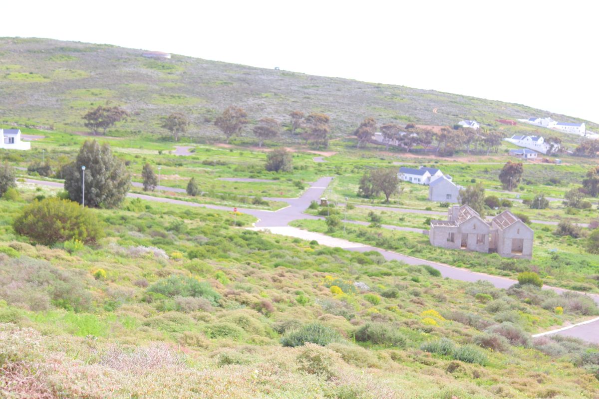 An elevated aerial view of a residential development area featuring paved roads, surrounding natural landscape, and scattered residential structures.