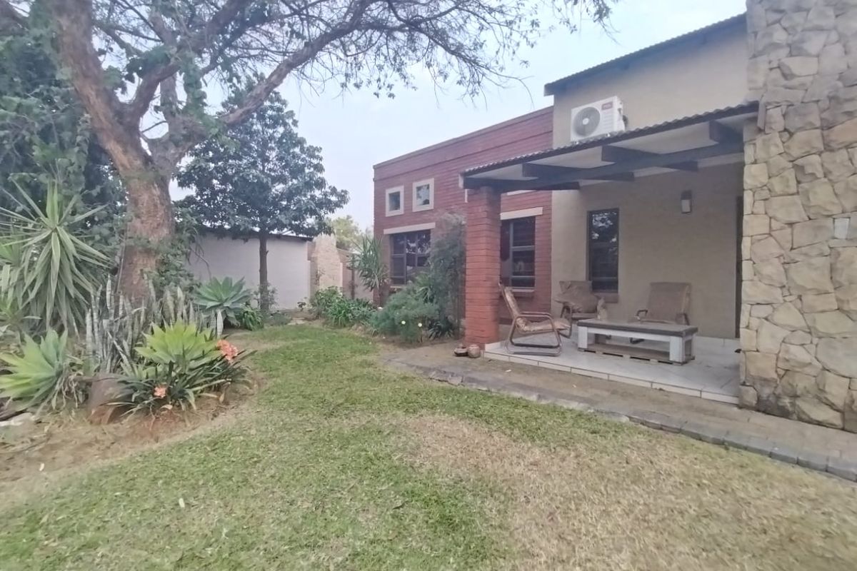 Rear view of the property featuring a covered patio with stone cladding, brick accents, and a landscaped garden area.