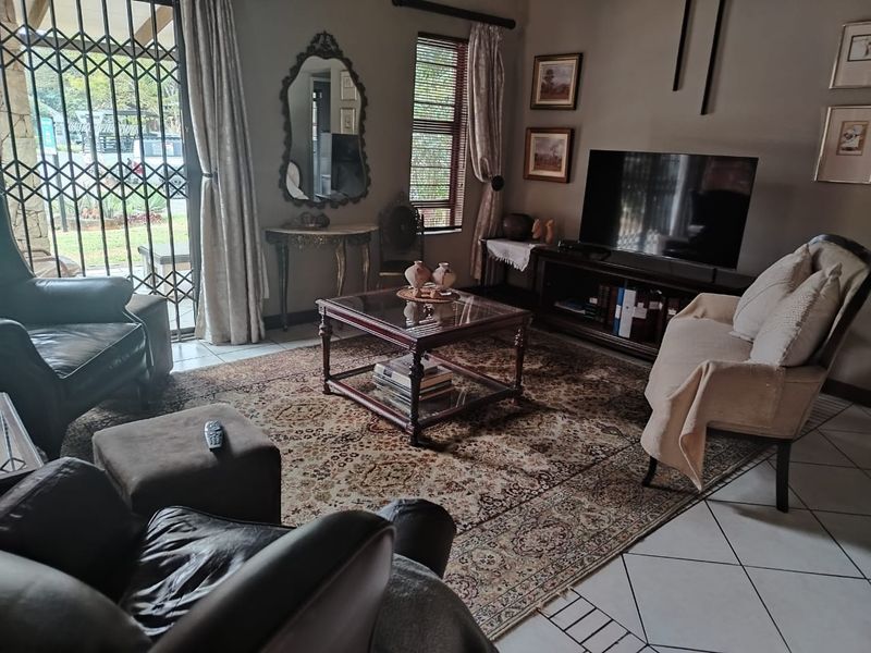 A comfortable living room featuring tiled flooring, a sliding door with a security gate, and venetian blinds, providing access to the outdoor area.