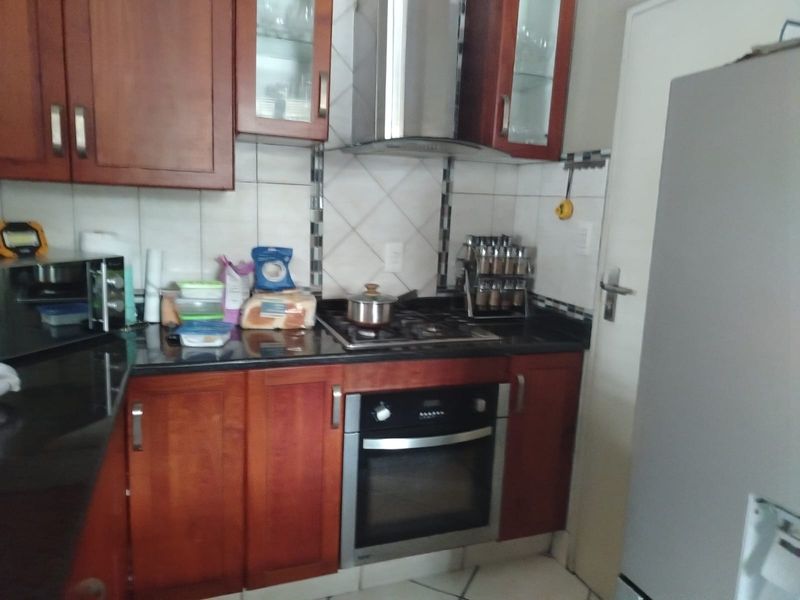 A functional kitchen featuring wooden cabinetry, granite countertops, a built-in oven, and a gas hob with an extractor fan.