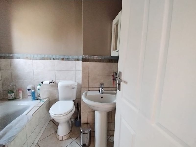 A functional bathroom featuring a pedestal basin, toilet, and built-in bathtub with tiled splashbacks and neutral wall finishes.
