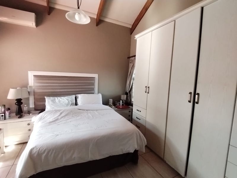 A bedroom featuring vaulted ceilings with exposed timber beams, built-in cupboards, and tiled flooring, equipped with a wall-mounted air conditioning unit.