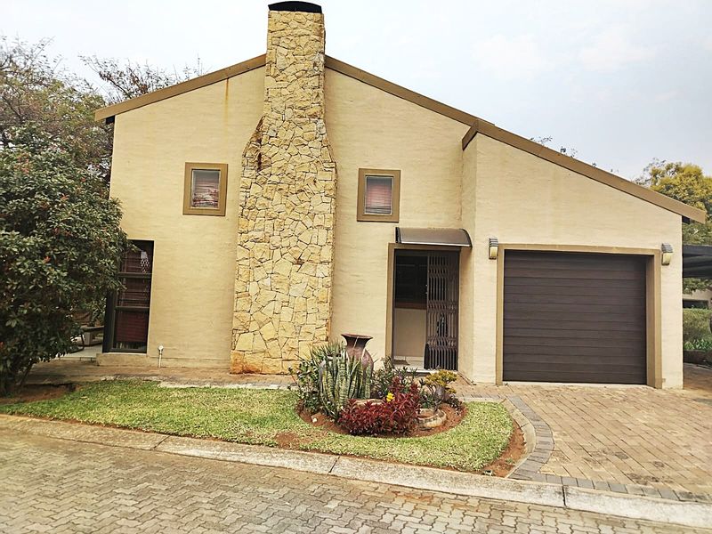 Front elevation of a house featuring a prominent stone chimney, paved driveway, single garage, and a small landscaped garden area.
