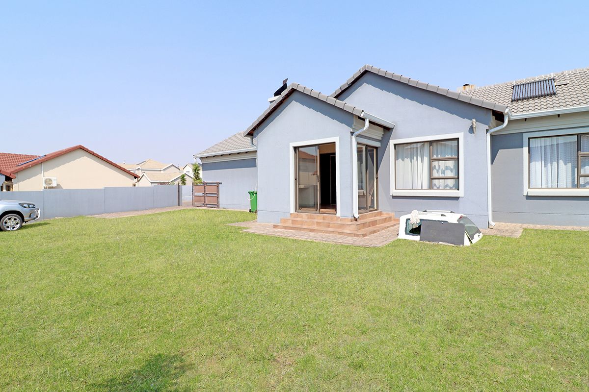 Rear view of the house featuring a paved patio area, tiled steps, and a well-maintained lawn within a fenced garden.