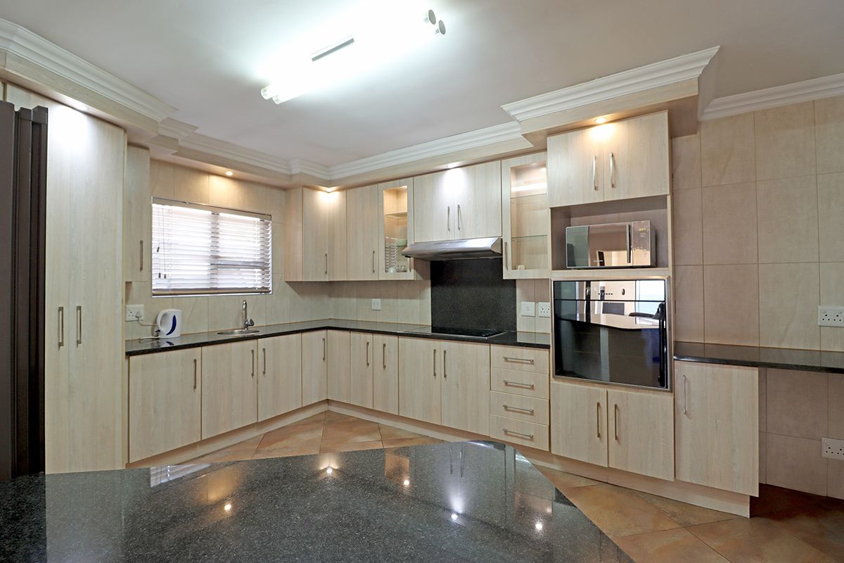 A well-maintained kitchen featuring light wood cabinetry, dark granite countertops, built-in oven, microwave, and extractor fan with tiled flooring.