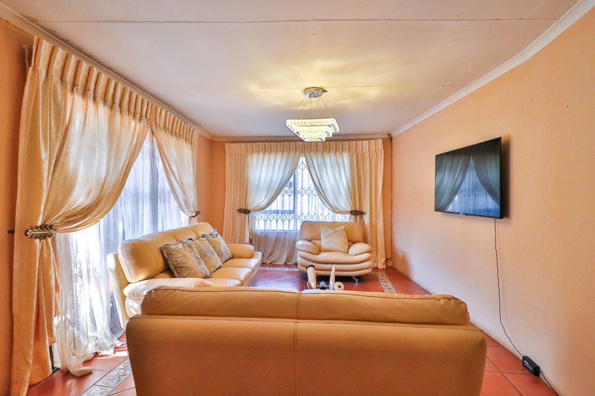 A comfortable living room featuring tiled flooring, a central light fixture, and large windows with security gates, offering a bright and functional space.