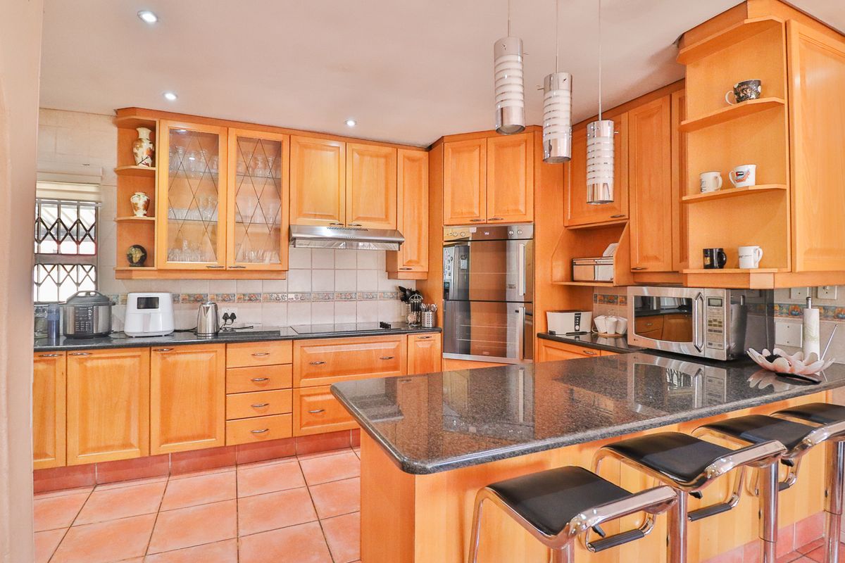 A functional kitchen featuring warm wooden cabinetry, granite countertops, built-in oven, extractor fan, and tiled flooring with a breakfast bar area.