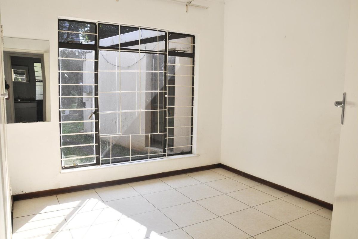 A bright, empty bedroom featuring tiled flooring, large windows with security bars, and a neutral interior finish.