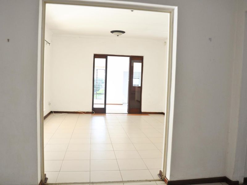 A bright, empty living area featuring neutral floor tiles and a doorway leading to an adjacent room.