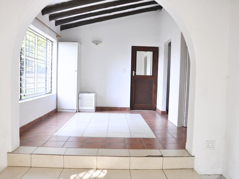 A sunlit room featuring exposed timber ceiling beams, tiled flooring, and an arched entryway, offering a versatile space with direct outdoor access.