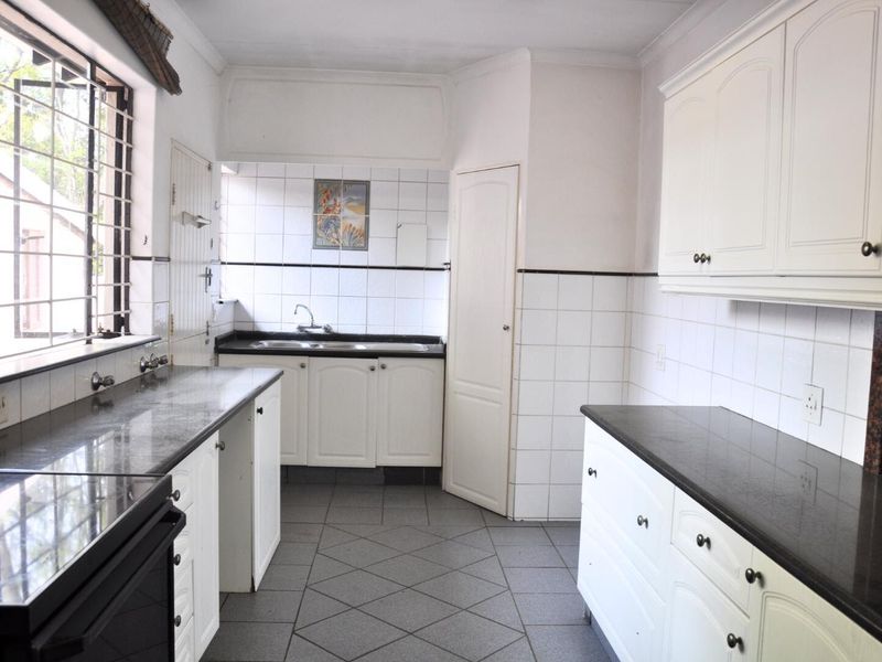 A functional kitchen featuring dark granite countertops, white cabinetry, tiled flooring, and a double sink with a window view.