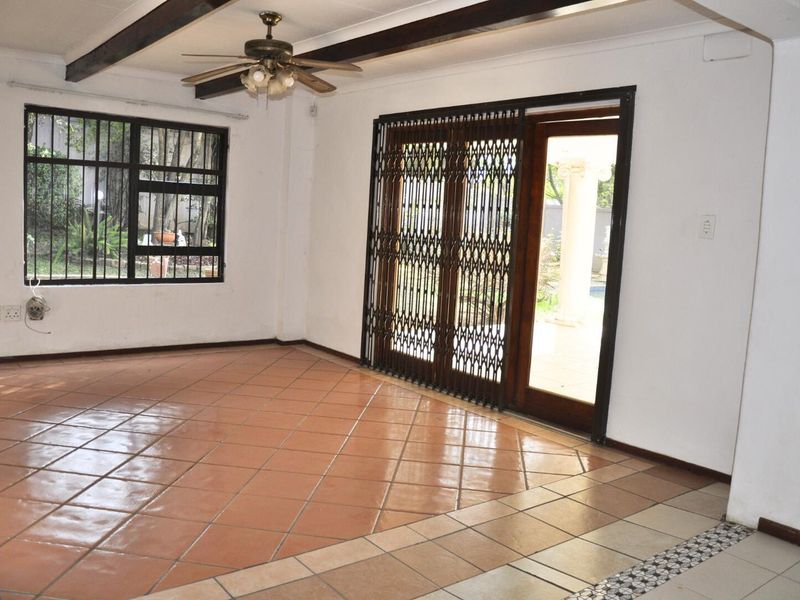 Spacious living area featuring terracotta floor tiles, exposed ceiling beams, a ceiling fan, and security gates leading to the outdoor patio.