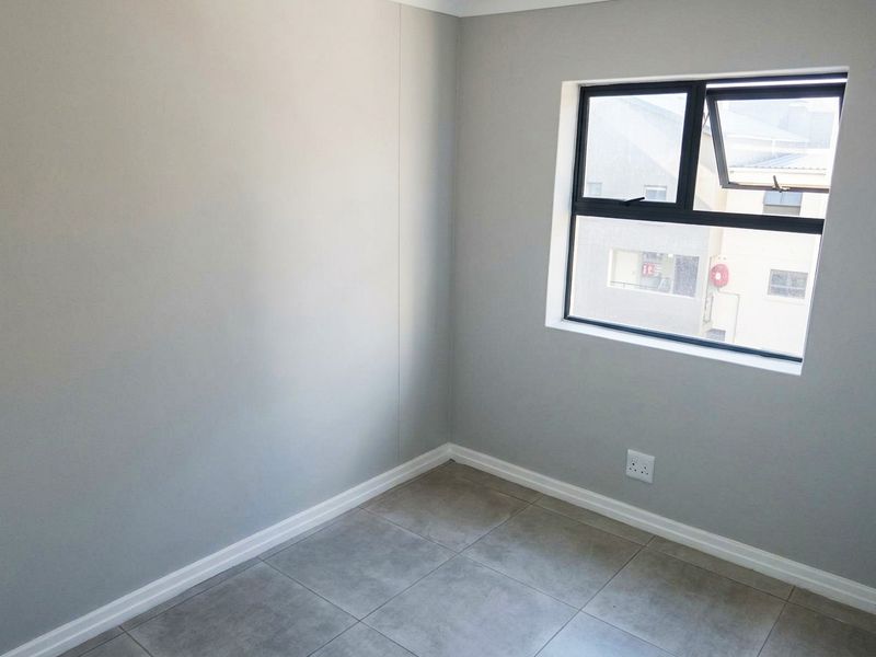 A clean, empty bedroom featuring neutral grey walls, modern tiled flooring, and a black aluminium window frame.