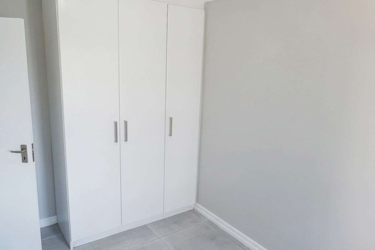 A clean, empty bedroom featuring neutral grey walls, modern tiled flooring, and a white built-in wardrobe with sleek handles.