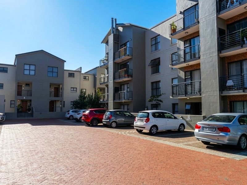 Exterior view of a multi-story apartment complex featuring a paved parking area and private balconies with metal railings.