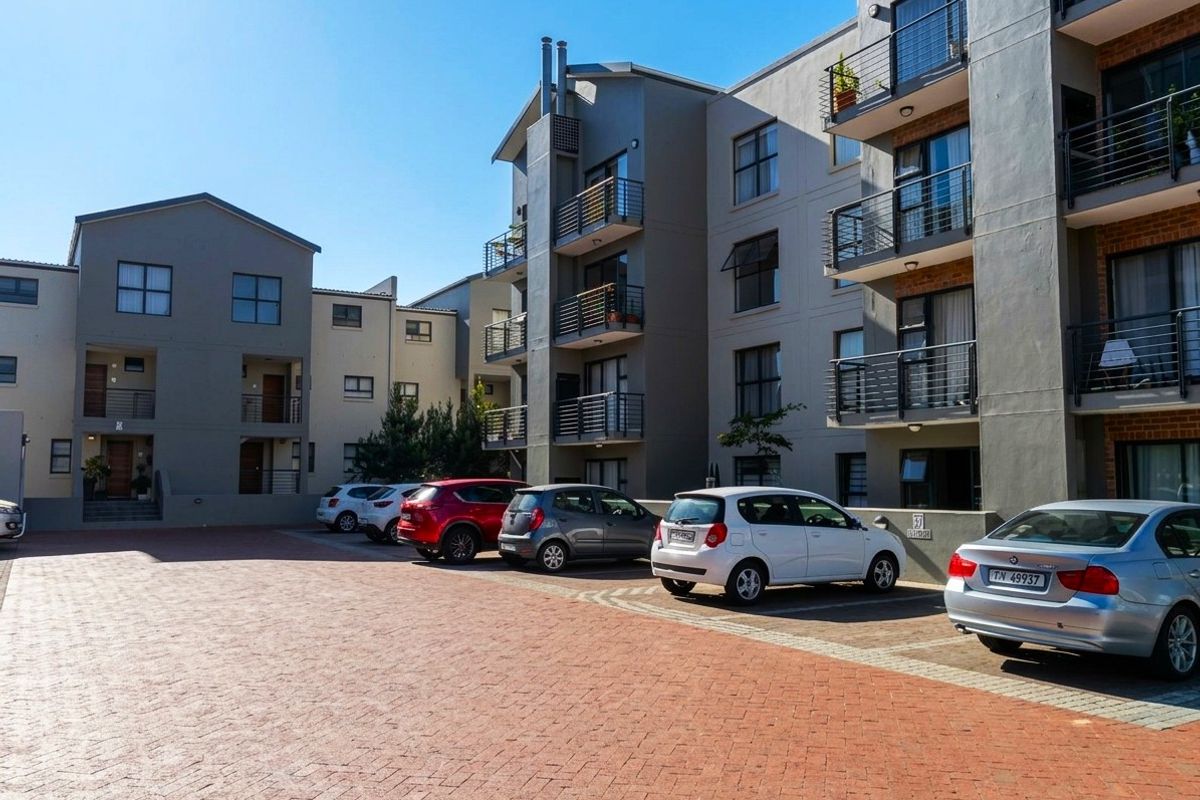 Exterior view of a multi-story apartment complex featuring a paved parking area and private balconies with metal railings.