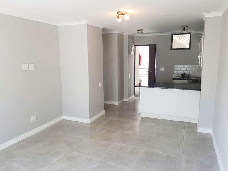 An open-plan living and kitchen area featuring neutral grey walls, large format floor tiles, and a modern kitchen island with a granite countertop.