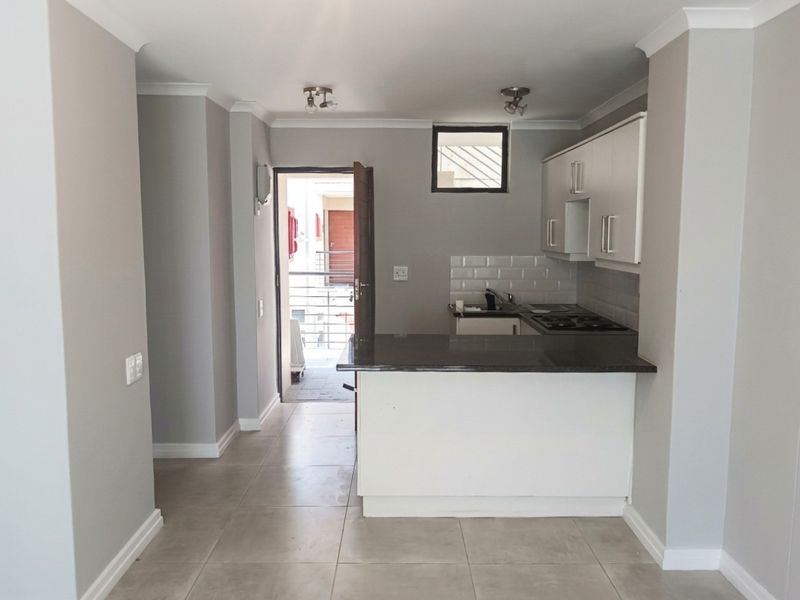 A clean, modern kitchen featuring granite countertops, white cabinetry, a subway tile backsplash, and a breakfast bar, leading directly to an outdoor balcony area.