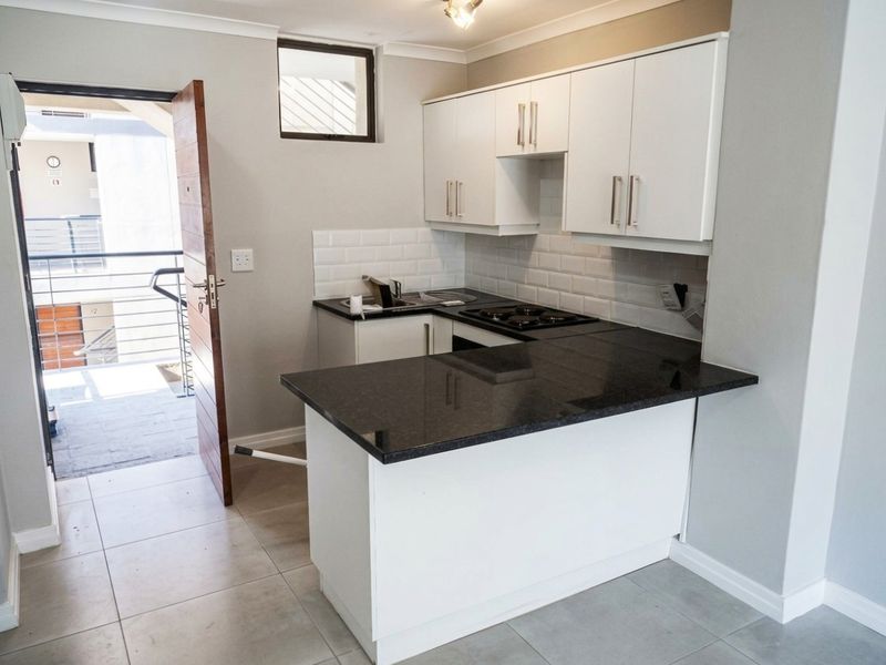 Modern kitchen featuring white cabinetry, dark granite countertops, subway tile backsplash, and integrated appliances, with direct access to an outdoor balcony area.