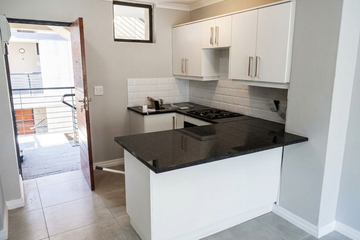 Modern kitchen featuring white cabinetry, dark granite countertops, subway tile backsplash, and integrated appliances, with direct access to an outdoor balcony area.