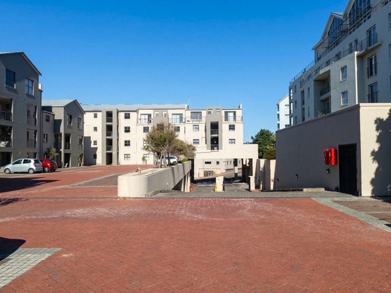 Exterior view of an apartment complex courtyard featuring paved driveways, access to underground parking, and multi-story residential buildings with balconies.