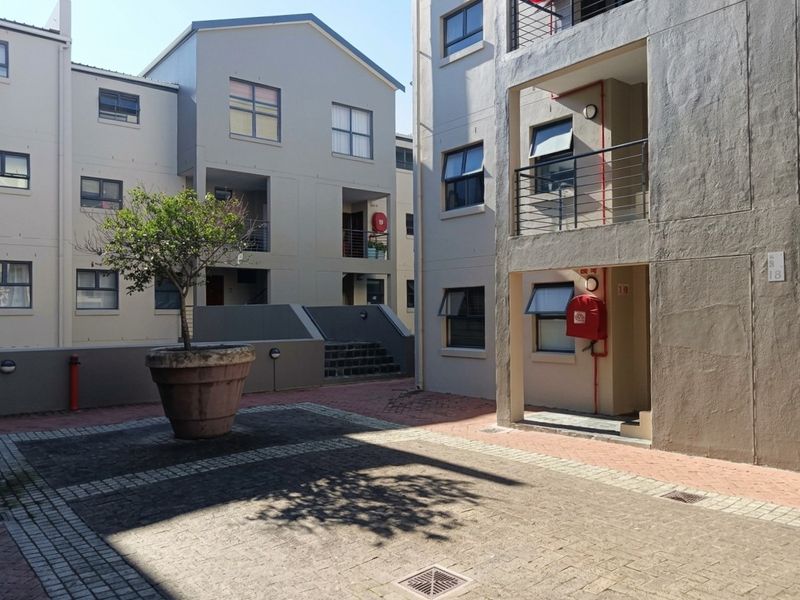 A view of the apartment complex courtyard featuring paved walkways, external staircases, and building access points with fire safety equipment.